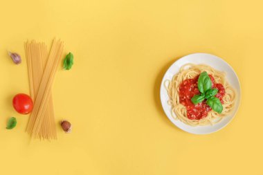 Spagetti makarna bolognese ve malzemelerin üzerine sarı arka plan, üstten görünüm. Domates sosu ve yaratıcı sarı zemin üzerine fesleğen ile makarna yemek tabağı.