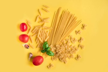 Fesleğen, domates ve sarı zemin üzerine sarımsak ile çeşitli pişmemiş çiğ makarna. İtalyan makarna: penne, farfalle, spagetti.