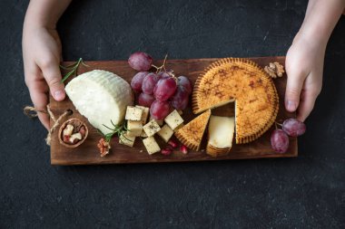 Peynir tabağı ile çeşitli peynirler, üzüm, fındık ve Peynirci'ye siyah arka plan üzerine elinde. İtalyan peynir ve meyve tabağı.