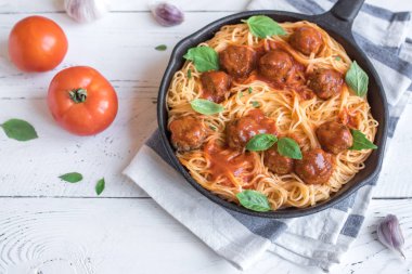 Köfte, domates sos ve taze fesleğen dökme demir tavada spagetti makarna. Beyaz ahşap arka plan kopya alanı ile sağlıklı ev yapımı İtalyan Makarna.