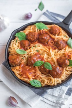 Köfte, domates sos ve taze fesleğen dökme demir tavada spagetti makarna. Beyaz ahşap arka plan kopya alanı ile sağlıklı ev yapımı İtalyan Makarna.