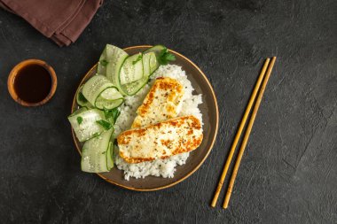 Pirinç ve salatalık salatası siyah arka plan, tofu biftek alanı kopyalayın. Kavrulmuş kızarmış tofu biftek ile sağlıklı vegan vejetaryen yemek yemek.