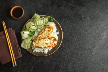 Pirinç ve salatalık salatası siyah arka plan, tofu biftek alanı kopyalayın. Kavrulmuş kızarmış tofu biftek ile sağlıklı vegan vejetaryen yemek yemek.