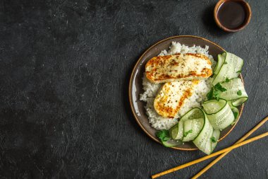 Pirinç ve salatalık salatası siyah arka plan, tofu biftek alanı kopyalayın. Kavrulmuş kızarmış tofu biftek ile sağlıklı vegan vejetaryen yemek yemek.