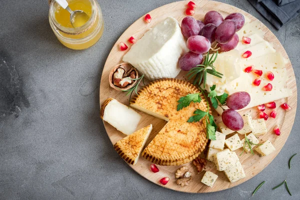 Cheese platter with assorted cheeses, grapes, nuts over gray stone background, copy space. Italian cheese and fruit platter.