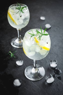 Alkol içki (cin tonik kokteyl) limon, biberiye ve rustik siyah taş tablo, kopya alanı buzda. Buzlu kokteyl içki limon ve otlar.
