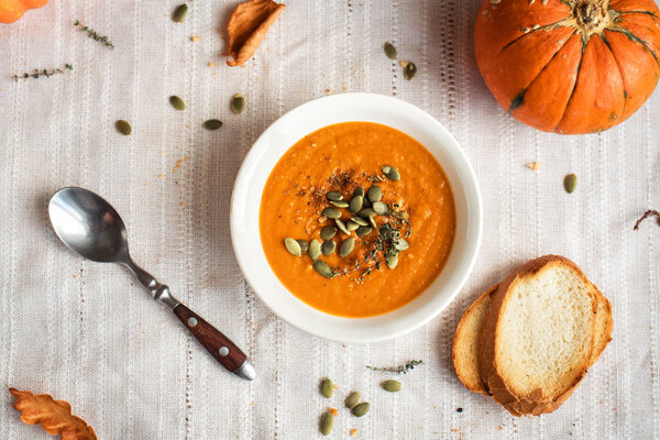 Pumpkin soup and organic pumpkins, top view. Seasonal autumn food - Spicy pumpkin soup with herbs and seeds.