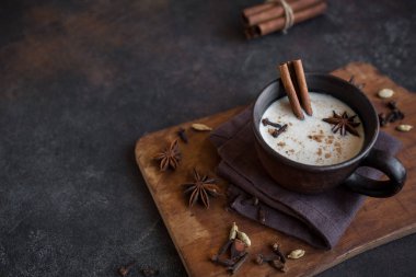 Geleneksel Hint masala chai çay malzemelerle seramik Kupası'nda. Rustik koyu arka plan üzerinde süt ile baharatlı siyah çay kapatır.
