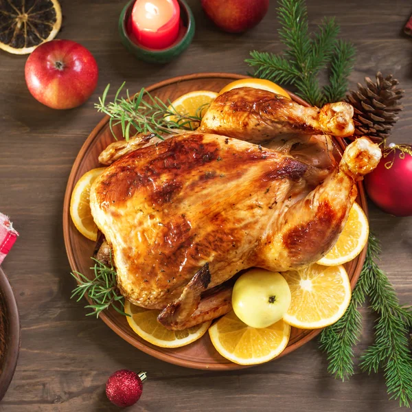Roasted Christmas Chicken or Turkey for Christmas Dinner. Festive decorated wooden table for Christmas Dinner with baked stuffed chicken.
