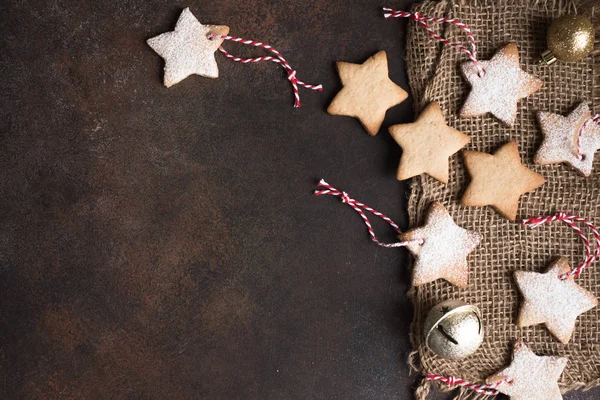 Christmas star shaped shortbread cookies with red ropes for Christmas tree decoration on dark rustic background, top view, copy space.