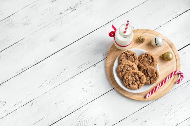 Çikolatalı kurabiye ve süt Noel Baba için. Geleneksel Noel ev yapımı kurabiye, şeker kamışı ve şişe süt ile Noel dekor Beyaz ahşap masa, üstten görünüm, Tarih alanı Kopyala.
