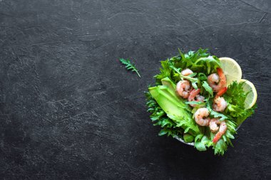 Siyah taş zemin üzerine avokado karides salatası alanı kopyalayın. Sağlıklı diyet yeşil salata karides (karides), avokado ve roka ile.