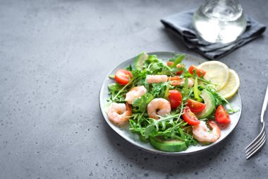 Roka ve domates gri taş zemin üzerine avokado karides salatası alanı kopyalayın. Sağlıklı diyet yeşil salata karides (karides), avokado, kiraz domates ve roka ile.