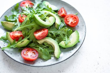 Yeşil salata ile dilimlenmiş avokado, domates ve taze roka beyaz taş masada kapatın. Sağlıklı beslenme vegan vejetaryen yaz sebze salatası gıda kavramı.