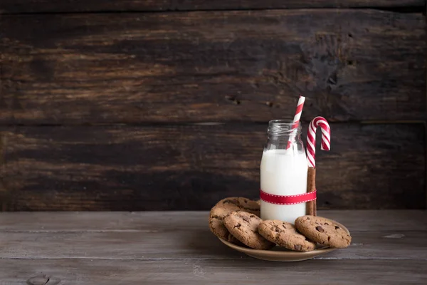 クッキーやサンタの牛乳 伝統的なクリスマスの自家製のチョコレート チップ クッキー キャンデー杖 素朴な木製のテーブルに赤いリボン ミルクの瓶をコピー スペース — ストック写真
