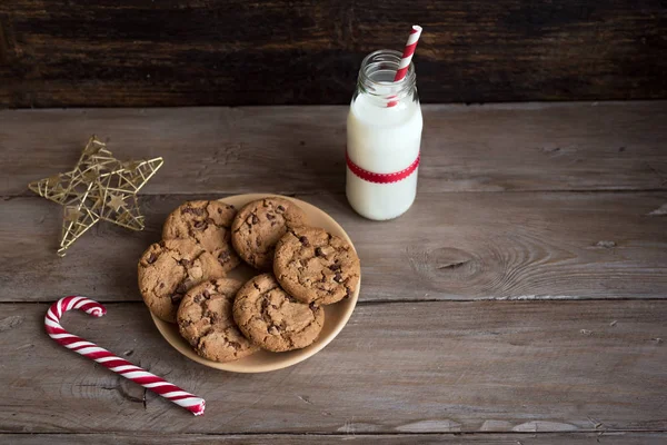 クッキーやサンタの牛乳 伝統的なクリスマスの自家製のチョコレート チップ クッキー キャンデー杖 素朴な木製のテーブルに赤いリボン ミルクの瓶をコピー スペース — ストック写真