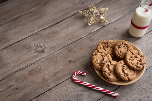 クッキーやサンタの牛乳 伝統的なクリスマスの自家製のチョコレート チップ クッキー キャンデー杖 素朴な木製のテーブル コピー領域のクリスマス装飾が施された牛乳瓶 — ストック写真