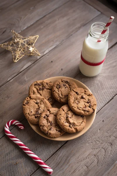 クッキーやサンタの牛乳 伝統的なクリスマスの自家製のチョコレート チップ クッキー キャンデー杖 素朴な木製のテーブル 上面の赤いリボンとミルクのボトル — ストック写真