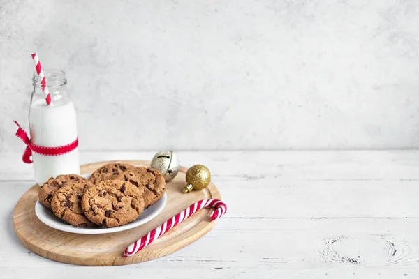 チョコレート チップ クッキーやサンタの牛乳 伝統的なクリスマス自家製クッキー キャンディの杖と白い木製のテーブルの上のクリスマスの装飾とミルクの瓶をコピー スペース — ストック写真