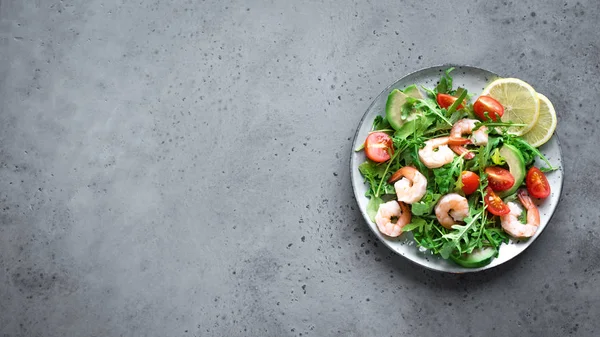 Avocado Shrimp Salad with Arugula and Tomatoes on grey stone background, copy space, top view, banner. Healthy diet green salad with Shrimps (prawns), avocado, cherry tomato and arugula.