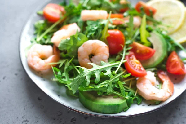 Avocado Shrimp Salad with Arugula and Tomatoes on grey stone background, close up. Healthy diet green salad with Shrimps (prawns), avocado, cherry tomato and arugula.
