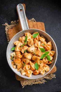 Farfalle makarna Tavuk ile domates sosu, fesleğen tavada. Tavuk İtalyan fiyonk makarna kopya alanı, ev yapımı İtalyan yemekleri ile siyah arka plan üzerinde.