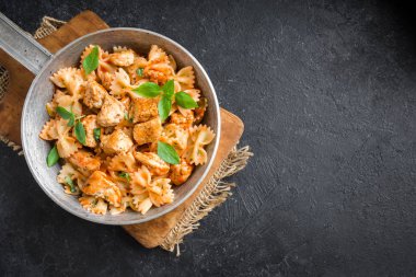 Farfalle makarna Tavuk ile domates sosu, fesleğen tavada. Tavuk İtalyan fiyonk makarna kopya alanı, ev yapımı İtalyan yemekleri ile siyah arka plan üzerinde.