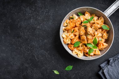 Farfalle makarna Tavuk ile domates sosu, fesleğen tavada. Tavuk İtalyan fiyonk makarna kopya alanı, ev yapımı İtalyan yemekleri ile siyah arka plan üzerinde.