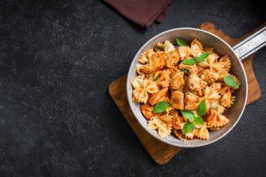 Farfalle makarna Tavuk ile domates sosu, fesleğen tavada. Tavuk İtalyan fiyonk makarna kopya alanı, ev yapımı İtalyan yemekleri ile siyah arka plan üzerinde.