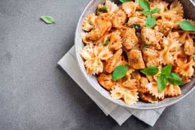 Farfalle makarna Tavuk ile domates sosu, fesleğen tavada. Tavuk İtalyan fiyonk makarna kopya alanı, ev yapımı İtalyan yemekleri ile beton arka plan üzerinde.