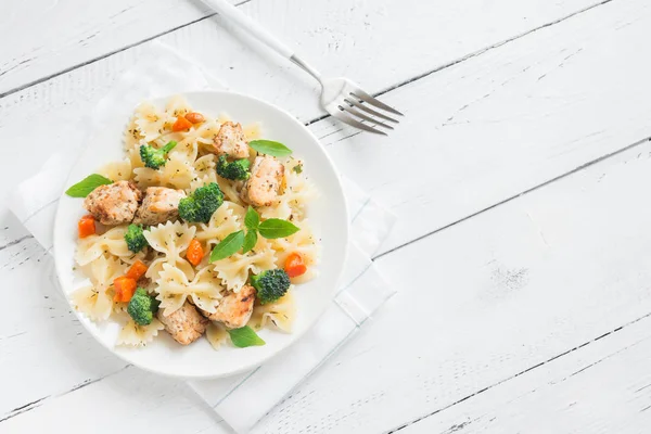 Farfalle pasta with chicken and vegetables. Pasta salad on white wooden background, copy space.