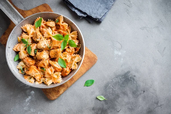 Farfalle pasta in tomato sauce with chicken,  basil in pan. Chicken italian bow tie pasta over concrete background with copy space, homemade italian food.