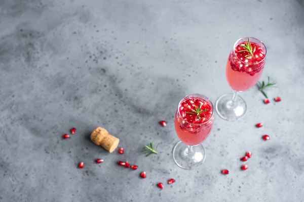 Pomegranate Champagne Mimosa Cocktail (Mocktail) with rosemary on concrete background, copy space. Mimosa Drink for Valentine Day or other holidays.