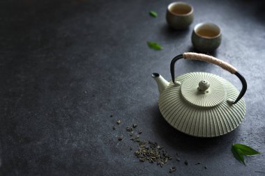 Çaydanlık ve Teacups siyah arka plan, kopya alanı üzerine. Geleneksel Asya çay seti - demir demlik ve yeşil çay ve çay yaprakları ile Seramik çay bardaklarından.