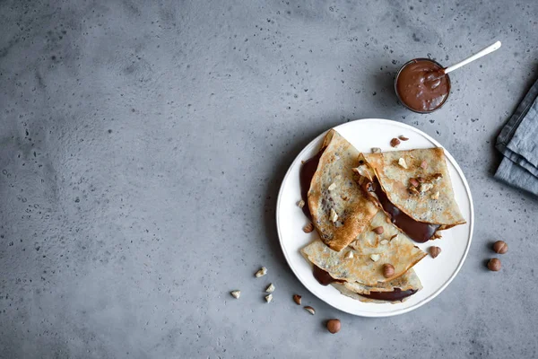 Crepes with chocolate spread and hazelnuts. Homemade thin crepes for breakfast or dessert on grey, copy space.