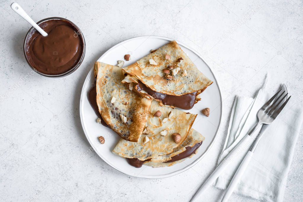 Crepes with chocolate spread and hazelnuts. Homemade thin crepes for breakfast or dessert on white, copy space.