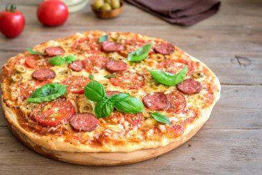 İtalyan Pizza domates, salam, yeşil zeytin, peynir ve fesleğen ile tahta masada bırakır. Taze ev yapımı Pizza, kopya alanı.