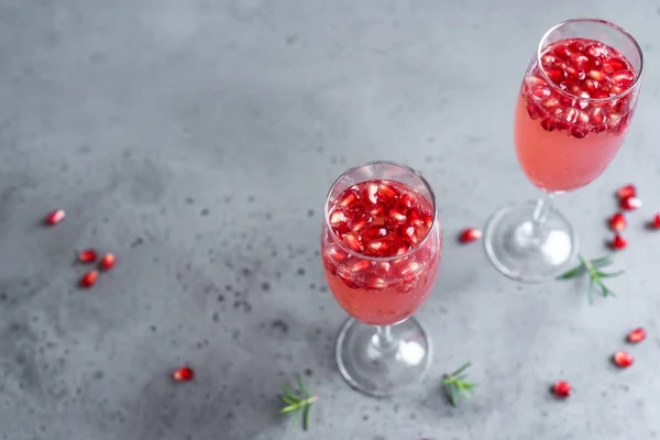 Pomegranate Champagne Mimosa Cocktail (Mocktail) with rosemary on concrete background, copy space. Mimosa Drink for Valentine Day or other holidays.