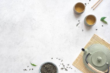 Green Tea Arrangement -  iron teapot and ceramic teacups with green tea and leaves. Traditional asian tea composition on white background, copy space, top view.