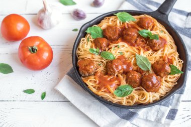 Köfte, domates sos ve taze fesleğen dökme demir tavada spagetti makarna. Beyaz ahşap zemin üzerinde sağlıklı ev yapımı İtalyan Makarna.