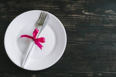 Romantik tablo ayarını beyaz tabak, modern çatal ve koyu siyah ahşap zemin, üstten görünüm, üzerine kırmızı kurdele ile alanı kopyalayın. Romantik akşam yemeği, dating, evlilik kavramı.