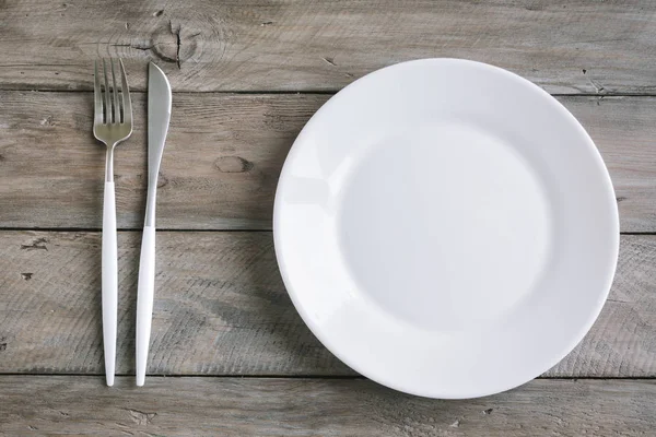 Empty table setting - plain white ceramic plate, cutlery on wooden table. Fasting concept, modern nordic style.