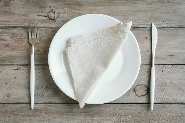 Empty table setting - plain white ceramic plate, cutlery on wooden table. Fasting concept, modern nordic style.