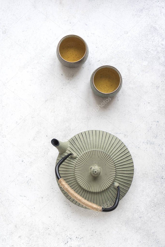 Green Tea Set -  iron teapot and ceramic teacups with green tea and leaves. Traditional asian tea composition on white background, copy space, top view.