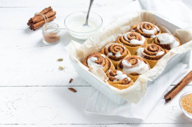 Rulo tarçın veya cinnabon, şekerli geleneksel tatlı çörekler Beyaz ahşap zemin üzerinde beyaz krema soslu ev yapımı tarifi.