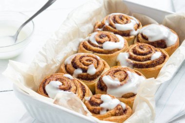 Rulo tarçın veya cinnabon, şekerli geleneksel tatlı çörekler Beyaz ahşap zemin üzerinde beyaz krema soslu ev yapımı tarifi.