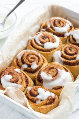 Rulo tarçın veya cinnabon, şekerli geleneksel tatlı çörekler Beyaz ahşap zemin üzerinde beyaz krema soslu ev yapımı tarifi.