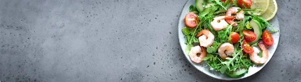 Avocado Shrimp Salad with Arugula and Tomatoes on grey stone background, banner, copy space. Healthy diet green salad with Shrimps (prawns), avocado, cherry tomato and arugula.