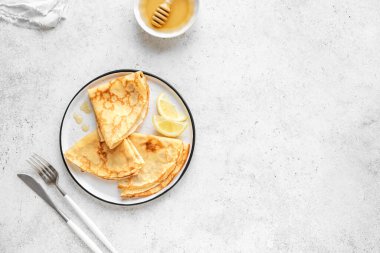 Beyaz arka planda limonlu ve ballı krepler, üst manzara, kopyalama alanı. Kahvaltı ya da tatlı için ince krep tarifi (Blini).