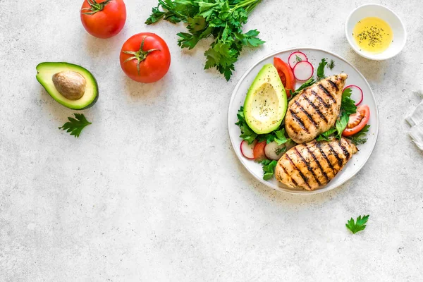 Healthy keto, ketogenic lunch menu with grilled chicken meat, avocado and organic veggies and greens. Roasted chicken breast, fillet and fresh vegetable salad, top view, copy space.